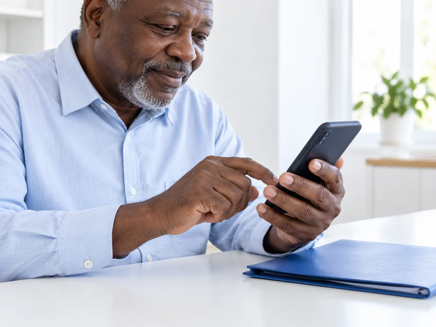 Illustration : homme ivoirien consultant son smartphone, un classeur de documents posé sur le bureau